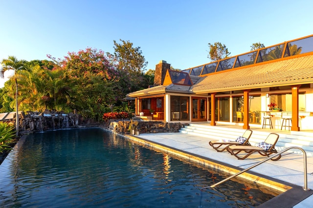 view of swimming pool with a bar, a patio, a water view, and pool water feature