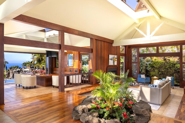 living room featuring beam ceiling, light wood-type flooring, high vaulted ceiling, and a skylight