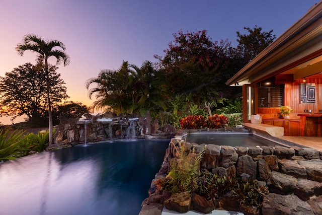 pool at dusk featuring pool water feature