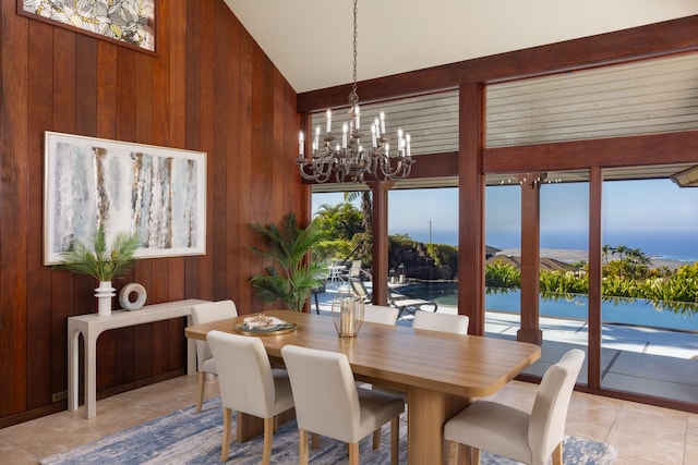 dining space with wood walls, a water view, light tile patterned flooring, and a chandelier