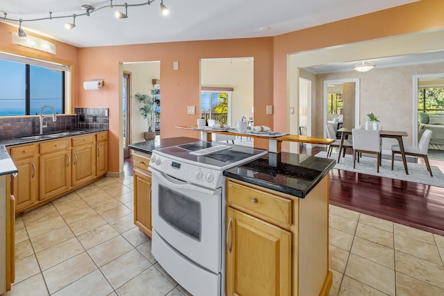 kitchen featuring backsplash, sink, light tile patterned floors, white electric range, and a kitchen island