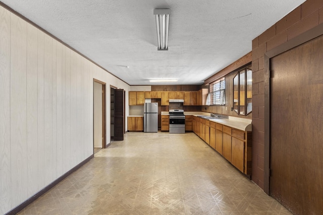 kitchen with a textured ceiling, appliances with stainless steel finishes, exhaust hood, wooden walls, and sink