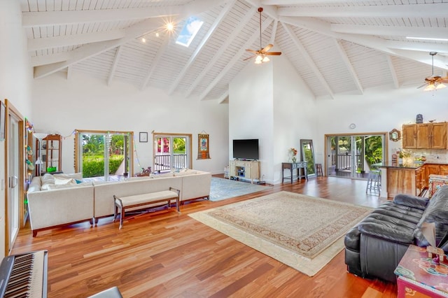 living room featuring beam ceiling, a skylight, high vaulted ceiling, and light hardwood / wood-style flooring