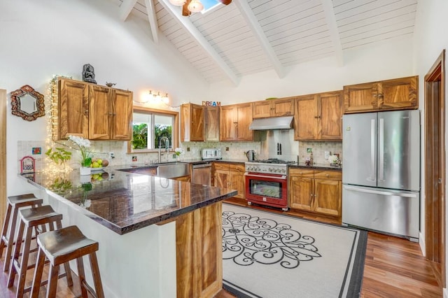 kitchen featuring high vaulted ceiling, backsplash, kitchen peninsula, a breakfast bar area, and appliances with stainless steel finishes