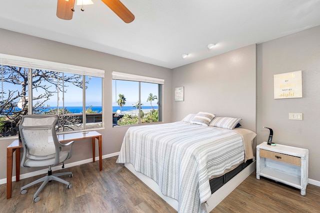 bedroom featuring dark hardwood / wood-style floors, ceiling fan, and a water view