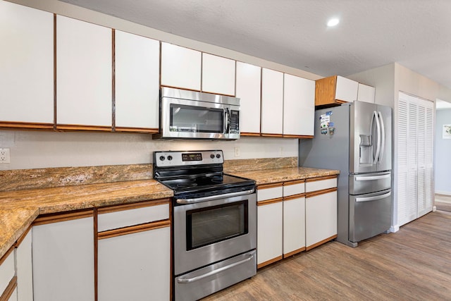 kitchen featuring light wood-type flooring, stainless steel appliances, white cabinetry, and light stone counters