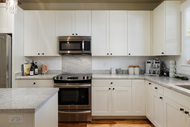 kitchen featuring light stone countertops, white cabinetry, backsplash, and appliances with stainless steel finishes