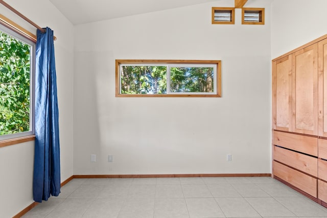 spare room with a wealth of natural light, light tile patterned floors, and vaulted ceiling