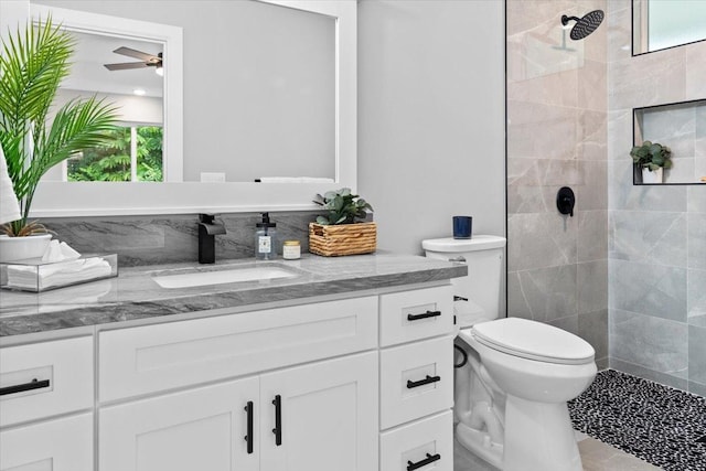 bathroom with a tile shower, ceiling fan, tile patterned floors, toilet, and vanity