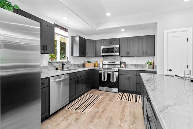 kitchen featuring sink, stainless steel appliances, light stone counters, light hardwood / wood-style floors, and gray cabinets