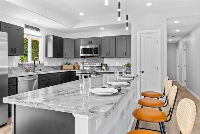 kitchen with light stone countertops, stainless steel appliances, sink, pendant lighting, and a center island