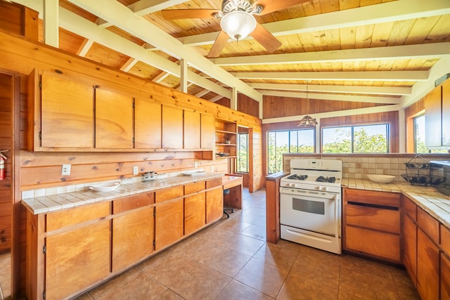 kitchen featuring white gas range, hanging light fixtures, lofted ceiling with beams, tile countertops, and wood walls