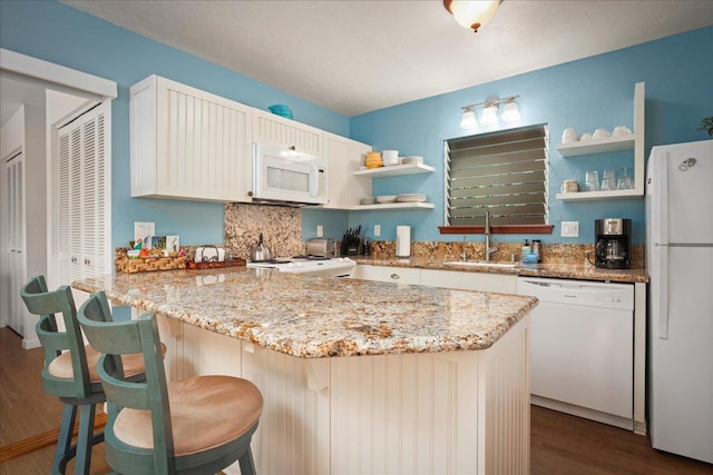 kitchen with dark hardwood / wood-style flooring, white appliances, a kitchen breakfast bar, and sink