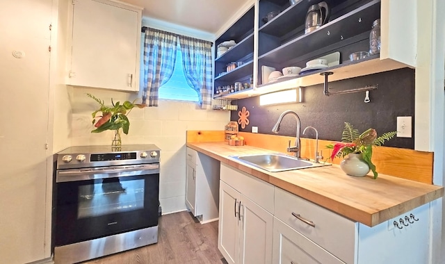 kitchen with butcher block countertops, stainless steel electric range oven, white cabinets, and light wood-type flooring