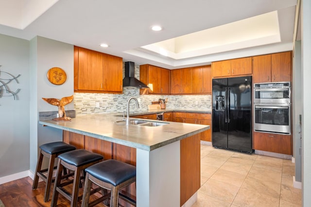 kitchen featuring kitchen peninsula, black refrigerator with ice dispenser, wall chimney exhaust hood, and stainless steel double oven