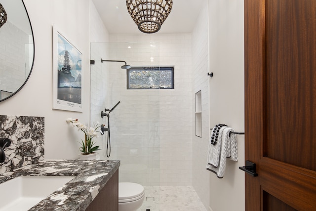 bathroom with toilet, vanity, tiled shower, and an inviting chandelier