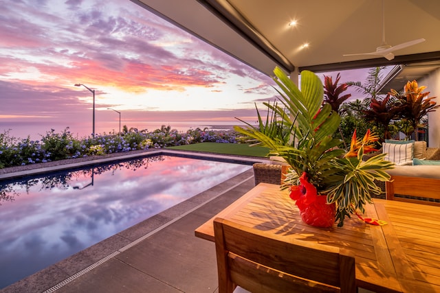 pool at dusk featuring ceiling fan and a water view