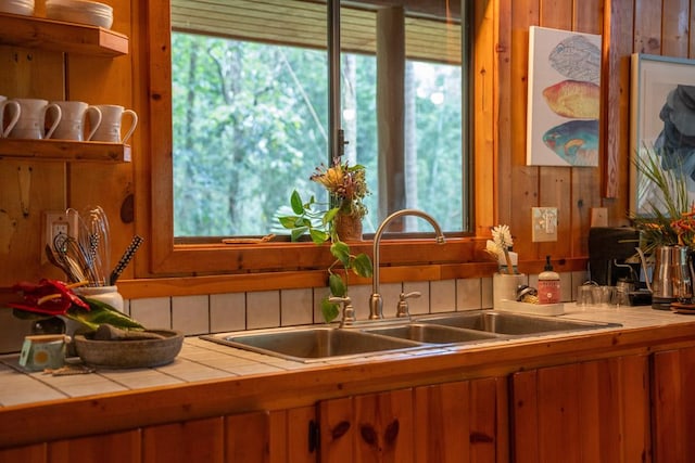 kitchen featuring tile countertops, plenty of natural light, sink, and wooden walls