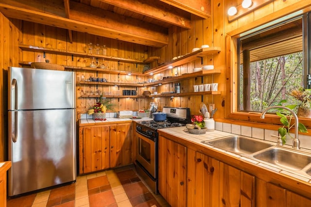 kitchen with wood walls, tile counters, stainless steel appliances, and sink