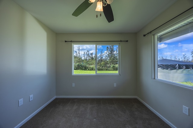 empty room featuring plenty of natural light, dark carpet, and ceiling fan