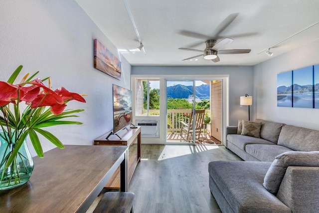 living room with ceiling fan, wood-type flooring, an AC wall unit, and track lighting