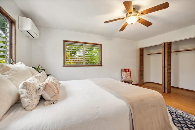 bedroom featuring a wall unit AC, ceiling fan, a closet, and light wood-type flooring