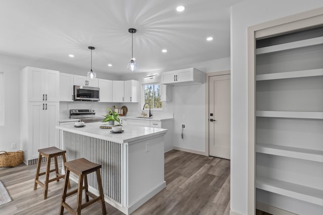 kitchen with sink, hanging light fixtures, a kitchen island, white cabinetry, and stainless steel appliances