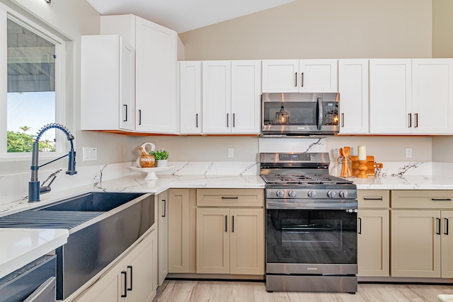 kitchen with sink, light stone countertops, stainless steel appliances, and vaulted ceiling