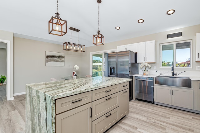 kitchen with sink, hanging light fixtures, stainless steel appliances, light stone counters, and a kitchen island