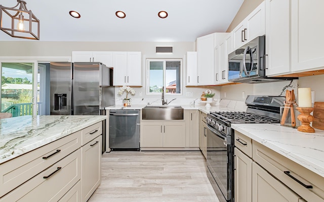 kitchen featuring light stone counters, stainless steel appliances, sink, decorative light fixtures, and white cabinets