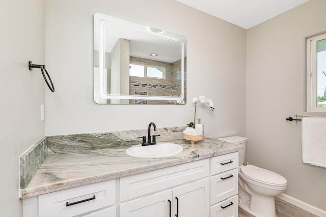 bathroom featuring a tile shower, hardwood / wood-style floors, vanity, and toilet