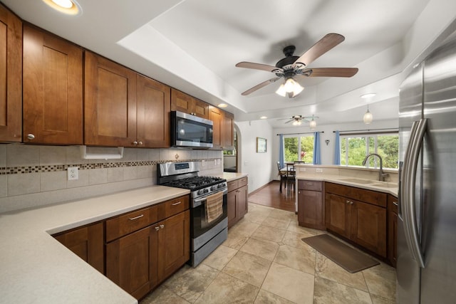 kitchen featuring appliances with stainless steel finishes, backsplash, a tray ceiling, ceiling fan, and sink