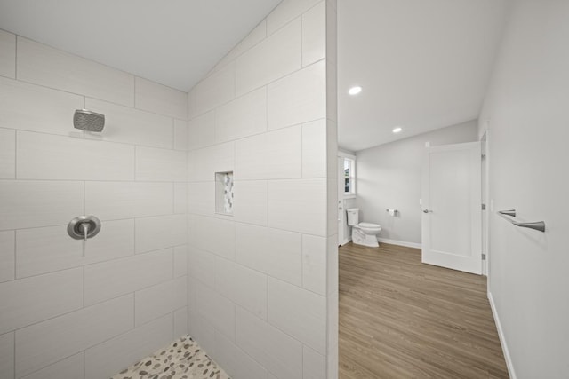 bathroom featuring hardwood / wood-style flooring, a tile shower, and vaulted ceiling