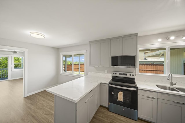 kitchen featuring kitchen peninsula, appliances with stainless steel finishes, gray cabinetry, sink, and hardwood / wood-style flooring