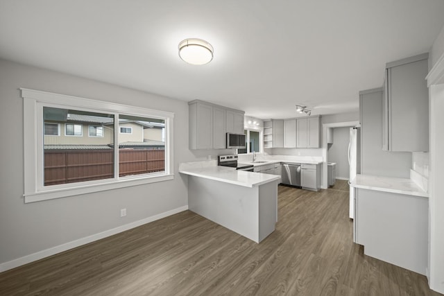 kitchen with gray cabinetry, sink, dark wood-type flooring, stainless steel appliances, and kitchen peninsula