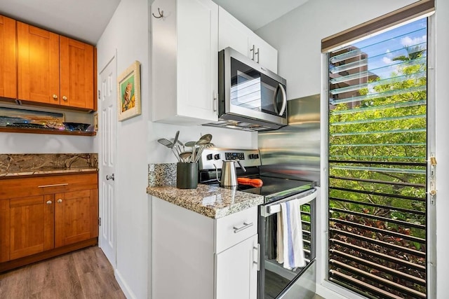 kitchen with white cabinets, light stone counters, stainless steel appliances, and light hardwood / wood-style flooring