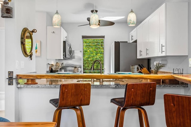 kitchen featuring white cabinets, ceiling fan, appliances with stainless steel finishes, decorative light fixtures, and a kitchen bar