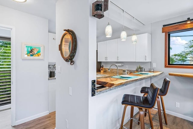 kitchen with white cabinets, a healthy amount of sunlight, pendant lighting, and light hardwood / wood-style flooring