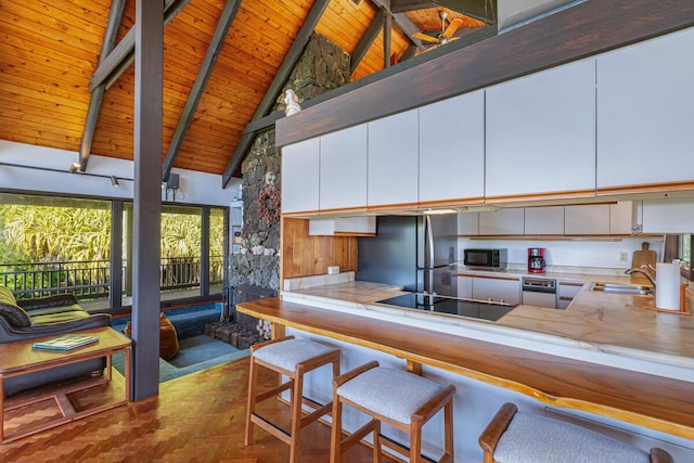 kitchen featuring beamed ceiling, high vaulted ceiling, kitchen peninsula, white cabinets, and appliances with stainless steel finishes