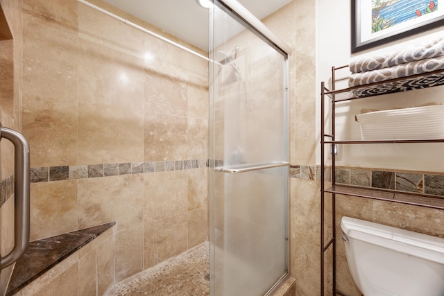 bathroom with toilet, a shower with door, and tile walls