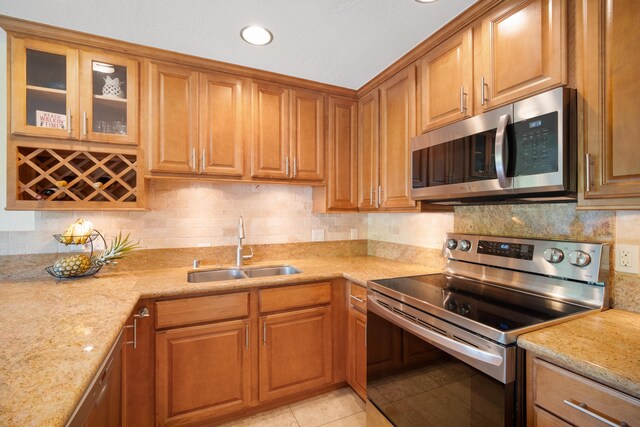 kitchen with light stone countertops, sink, stainless steel appliances, tasteful backsplash, and light tile patterned flooring