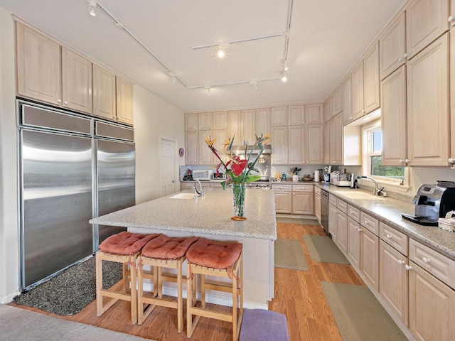 kitchen with a breakfast bar, stainless steel appliances, sink, a center island with sink, and light hardwood / wood-style floors