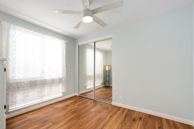 unfurnished bedroom featuring multiple windows, ceiling fan, a closet, and hardwood / wood-style flooring