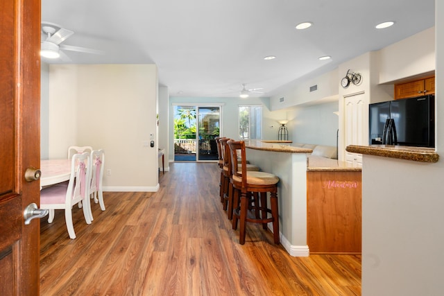 kitchen featuring ceiling fan, dark hardwood / wood-style floors, kitchen peninsula, a breakfast bar area, and black fridge with ice dispenser