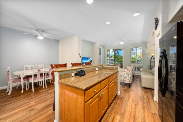 kitchen with black refrigerator, a kitchen bar, light stone counters, a center island, and light hardwood / wood-style floors