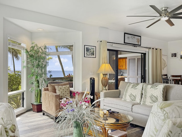 living room with ceiling fan, a water view, and wood-type flooring