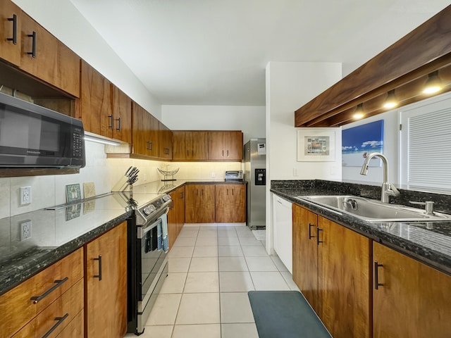 kitchen featuring sink, light tile patterned floors, appliances with stainless steel finishes, dark stone countertops, and tasteful backsplash