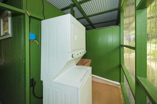 washroom with wood walls, plenty of natural light, and stacked washer and clothes dryer