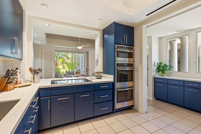 kitchen with black electric stovetop, a tray ceiling, double oven, ceiling fan, and blue cabinetry