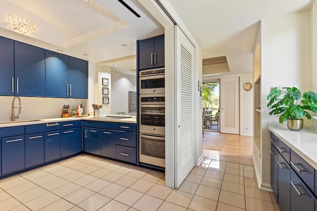 kitchen with backsplash, sink, blue cabinetry, light tile patterned floors, and stovetop